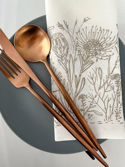 Eclectic Fynbos oatmeal botanical print airlaid napkin on a grey plate with copper cutlery