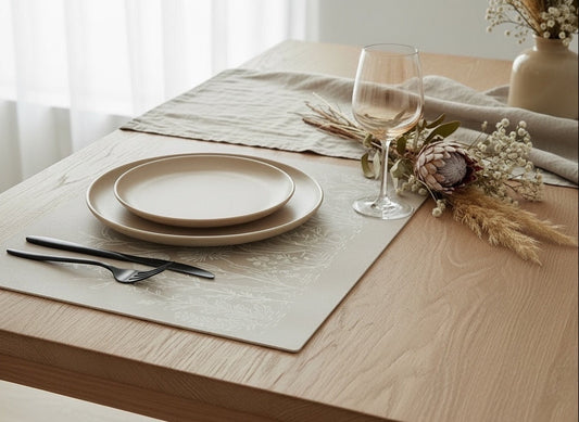 Eclectic Fynbos Oatmeal reusable placemats with white botanical linework on a wooden table with plates and cutlery.