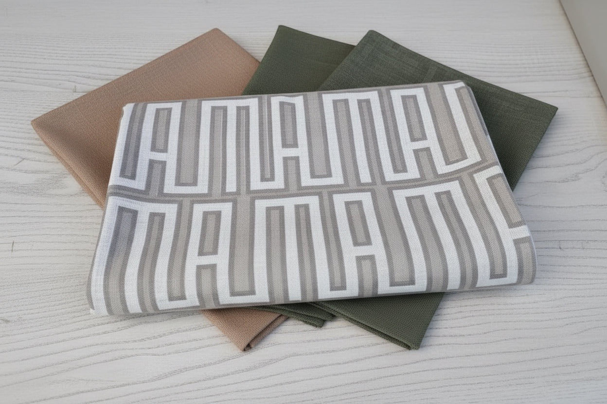 Eclectic geometric linen-look tablecloths in natural, green, and beige folded on a white wooden table.
