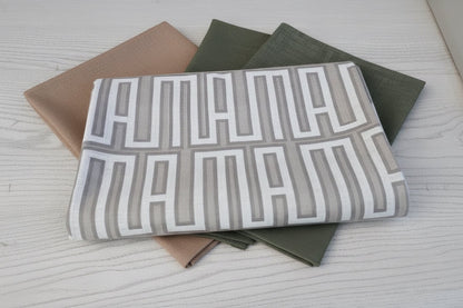 Eclectic geometric linen-look tablecloths in natural, green, and beige folded on a white wooden table.