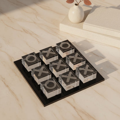 Eclectic glass noughts and crosses game with clear glass pieces on a sleek black base, styled on a marble table.