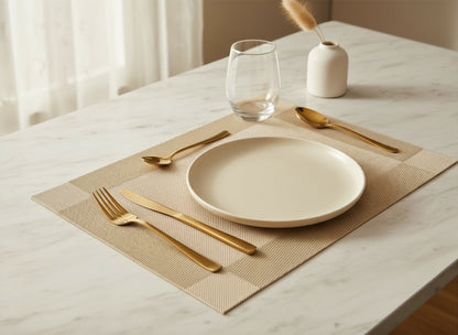Eclectic gold woven PVC rectangular placemat set on a marble table with a white plate and gold cutlery.