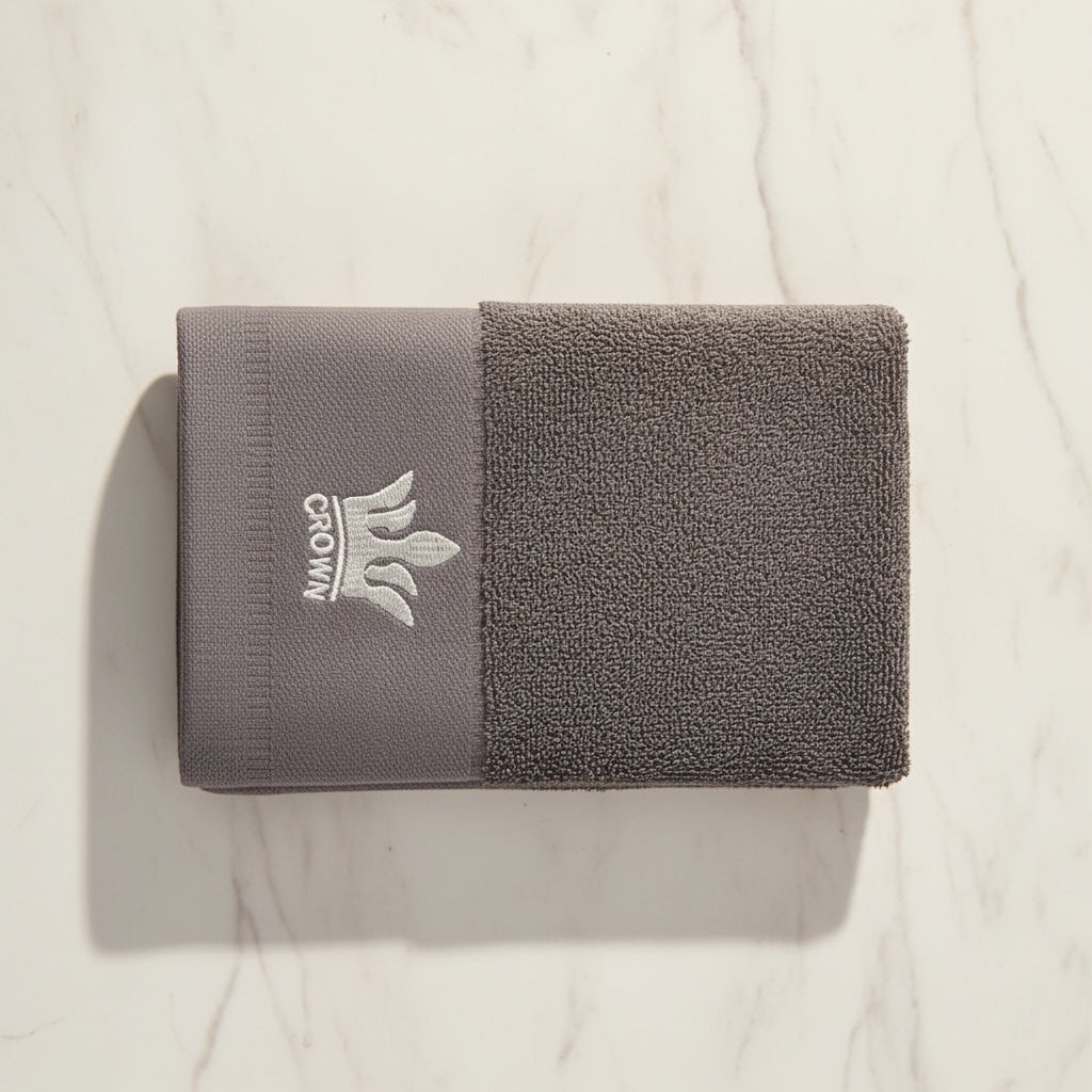 Eclectic grey cotton guest towel with an elegant embroidered crown detail on a marble surface.