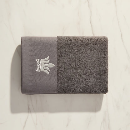 Eclectic grey cotton guest towel with an elegant embroidered crown detail on a marble surface.