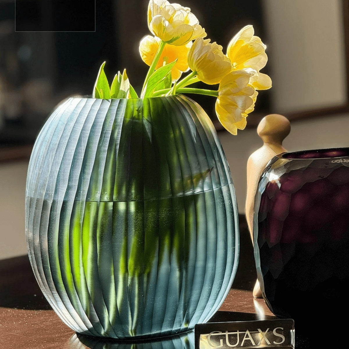 Eclectic Guaxs Patara round mouth-blown glass vase in ocean blue with a hand-cut pleated texture holding yellow tulips