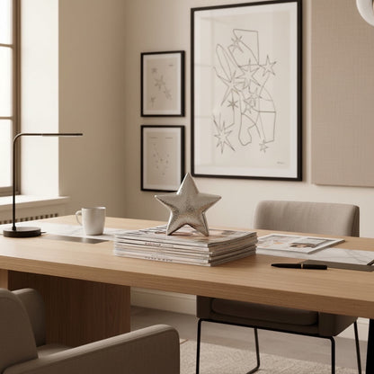 Eclectic hammered silver ceramic star sculpture displayed on a stack of magazines on a modern wooden office desk.