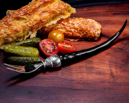 Eclectic Impondo Zulu pickle fork with a black resin horn-style handle and pewter detail on a wooden serving board.