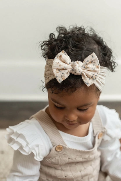 Eclectic ivory baby headband with a delicate floral print and a soft bow, worn by a baby with curly hair.