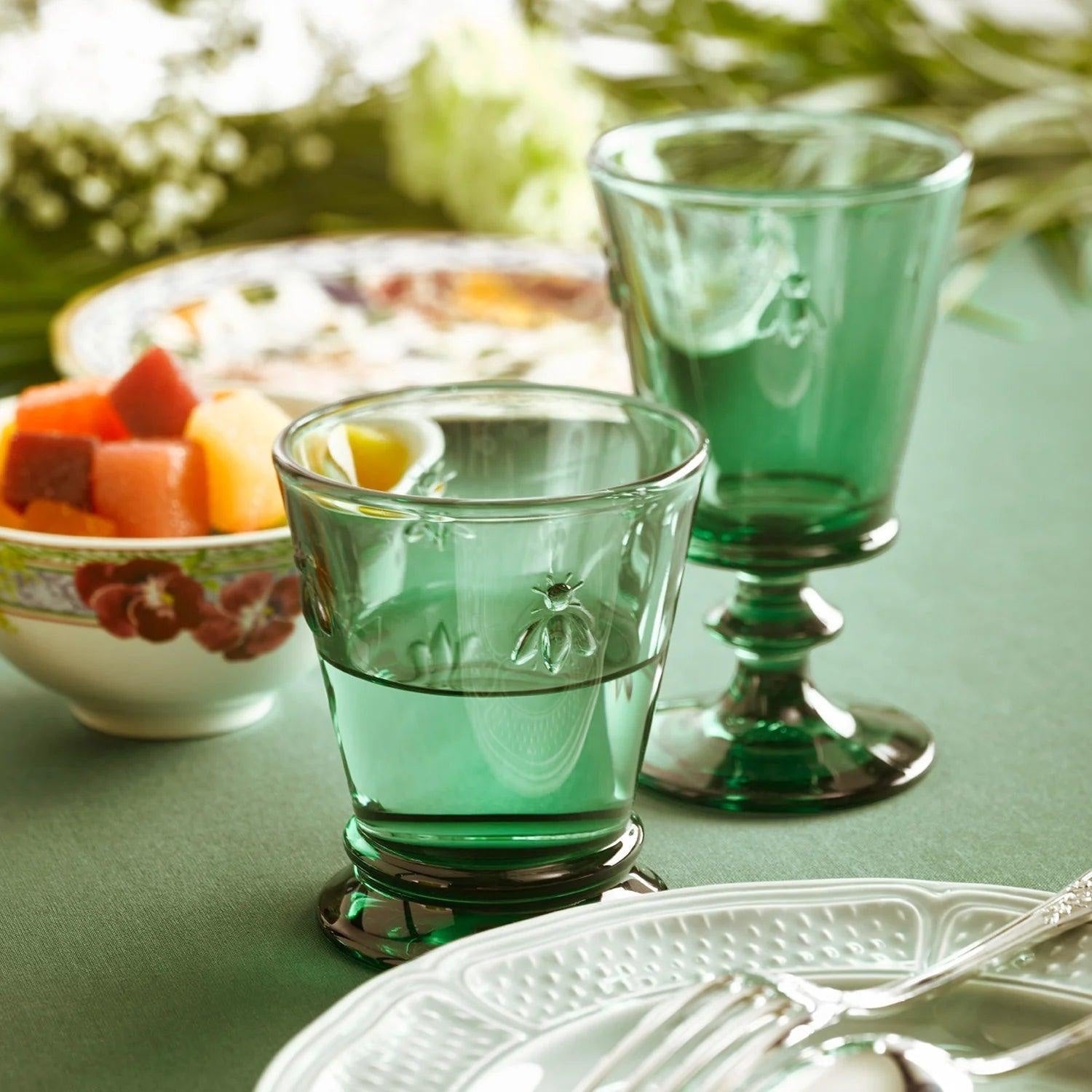 Eclectic La Rochère Abeille green pressed glass tumblers with Napoleonic bee motif on a dining table setting.