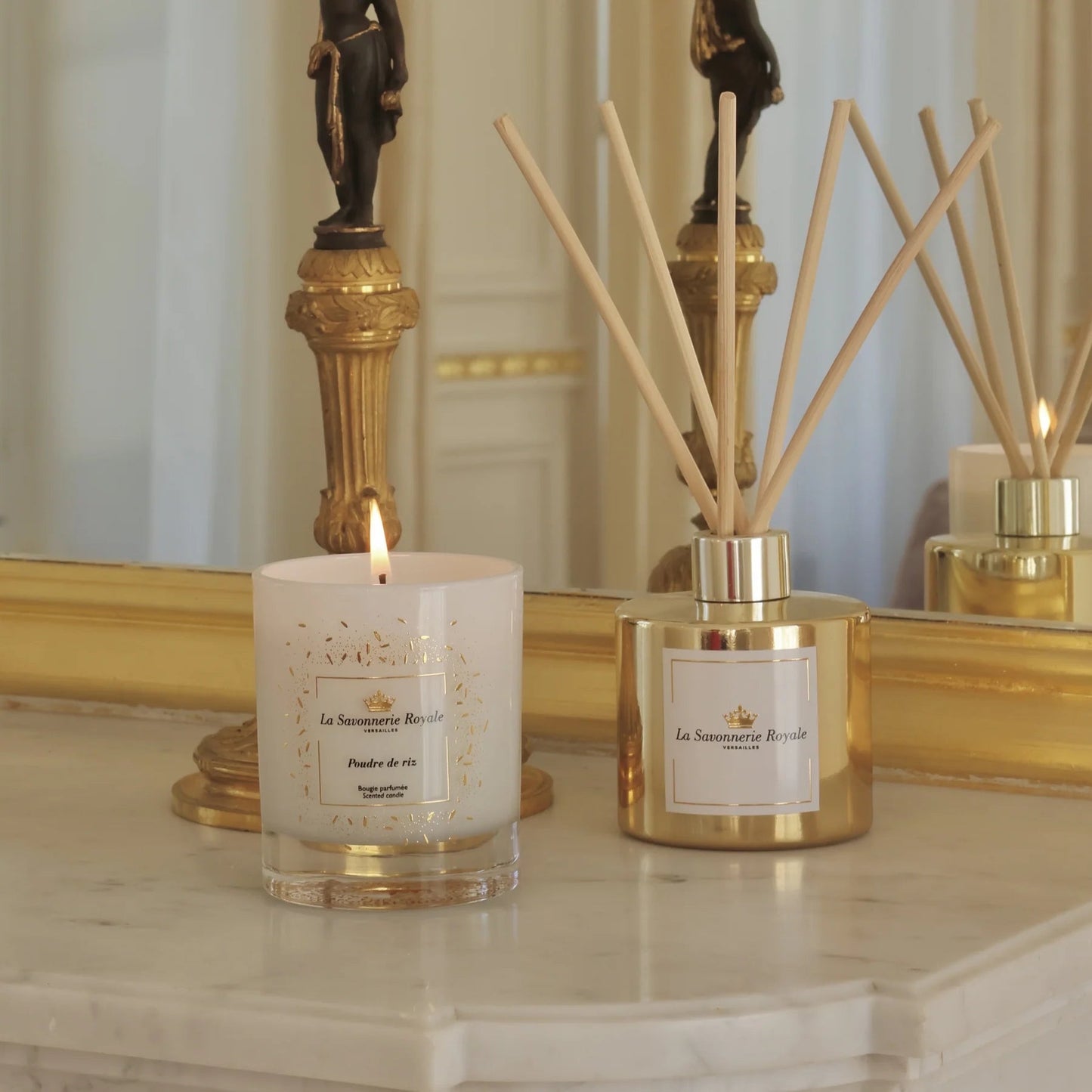 Eclectic La Savonnerie Royale Poudre de Riz candle in a glass vessel next to a gold reed diffuser on a marble surface.