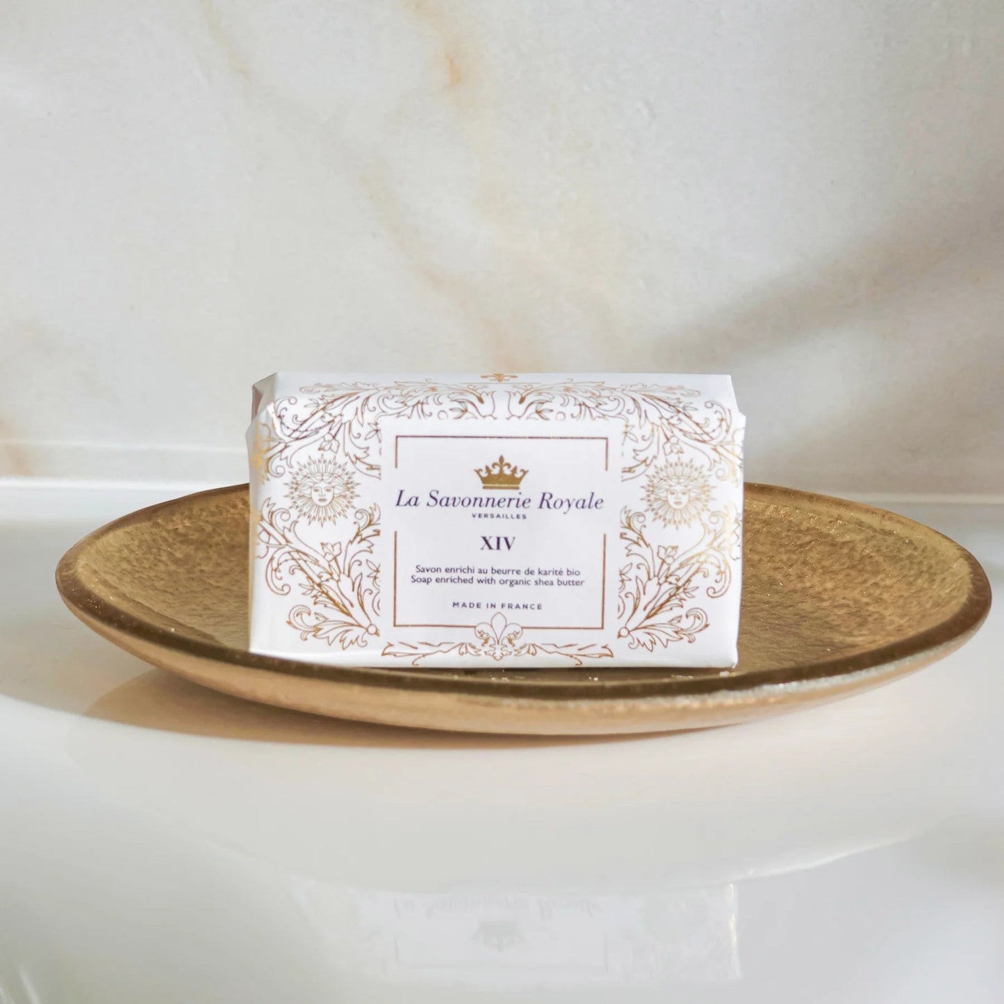Eclectic La Savonnerie Royale XIV soap bar in ornate white and gold packaging resting on a gold dish.
