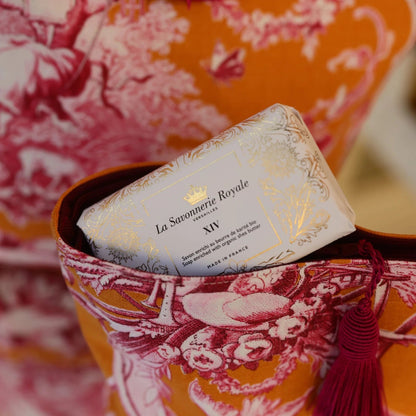 Eclectic La Savonnerie Royale XIV soap bar in ivory packaging with gold foil details tucked in a patterned fabric bag.