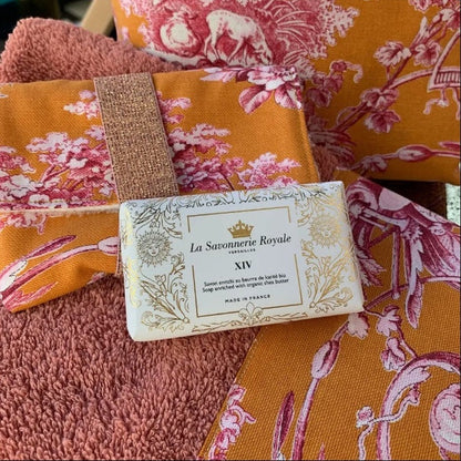 Eclectic La Savonnerie Royale XIV soap bar with Fleur-de-lys embossing, set against orange floral fabric and a towel.