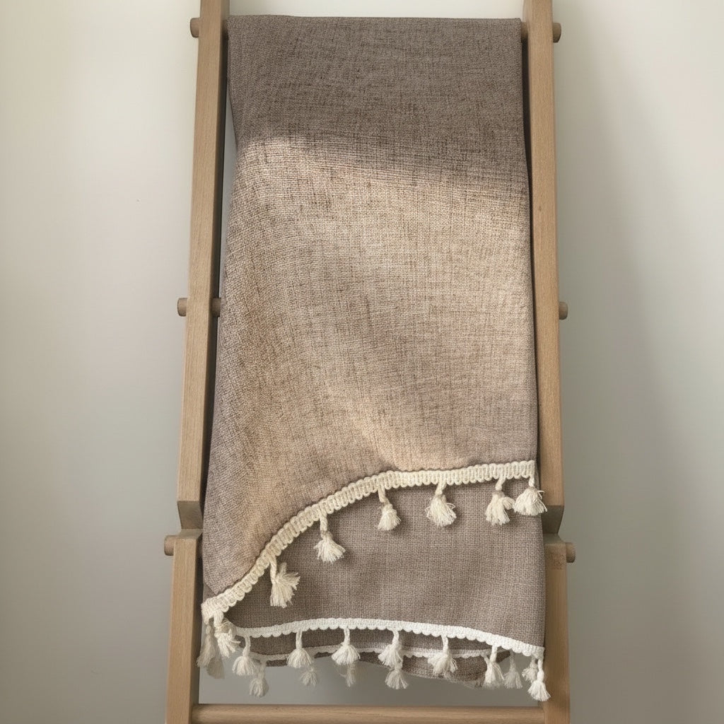 Eclectic light coffee linen blend tablecloth with cream tassel trim draped over a wooden ladder