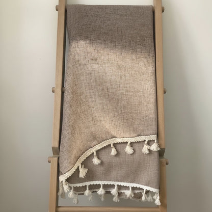 Eclectic light coffee linen blend tablecloth with cream tassel trim draped over a wooden ladder