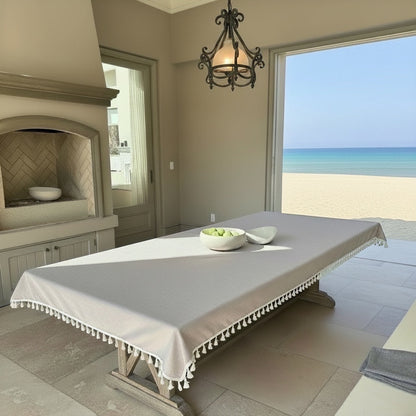 Eclectic light coffee linen blend waterproof tablecloth with tassel trim on a dining table overlooking the beach.
