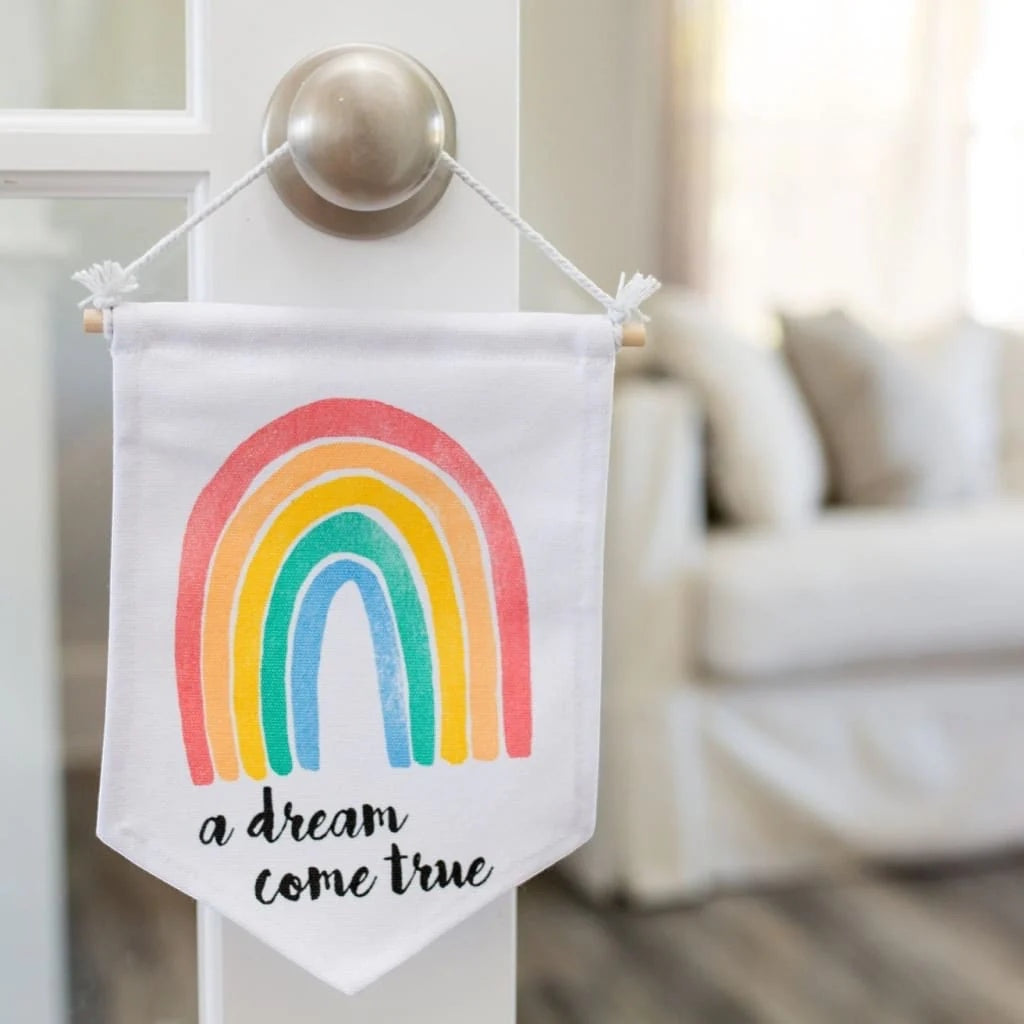 Eclectic Lulujo rainbow nursery wall banner with wooden hanger hanging on a door handle