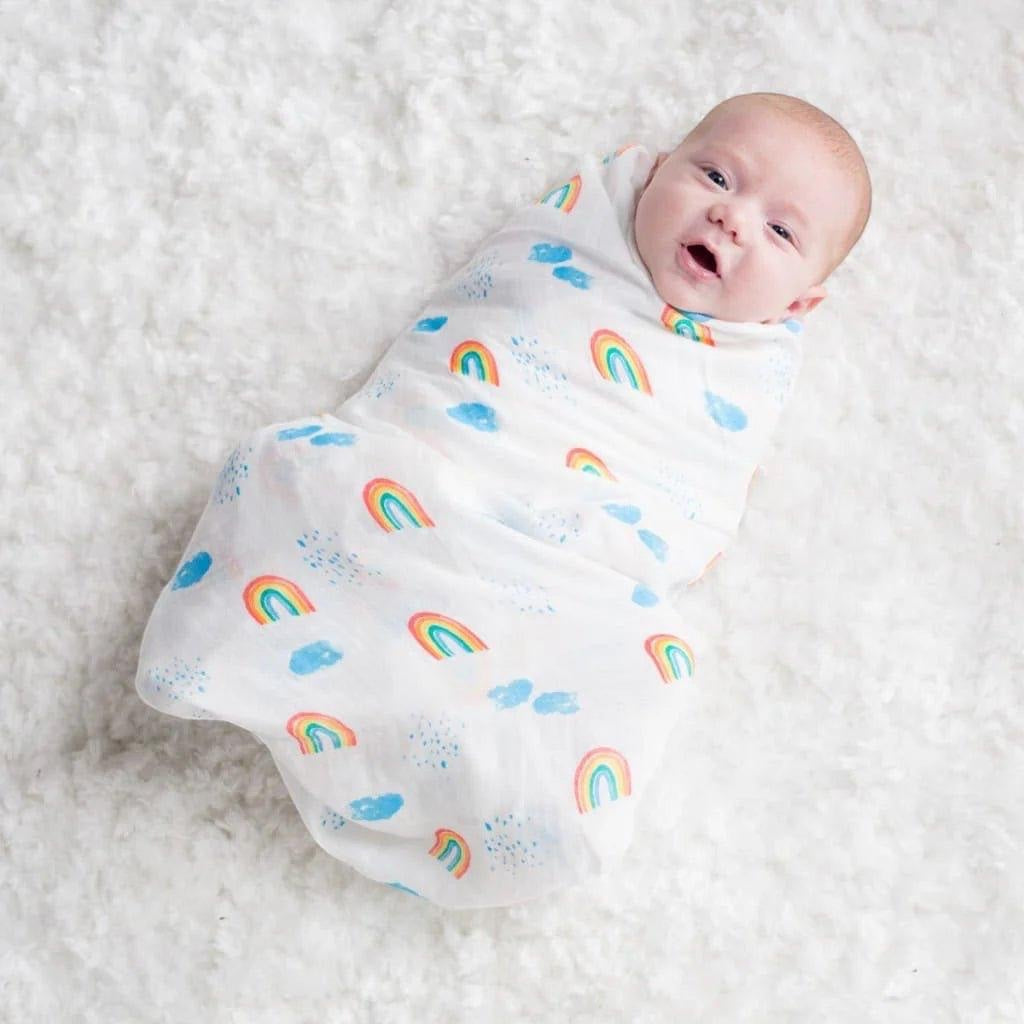 Eclectic Lulujo baby swaddled in a white cotton muslin blanket featuring a colourful rainbow and sky print