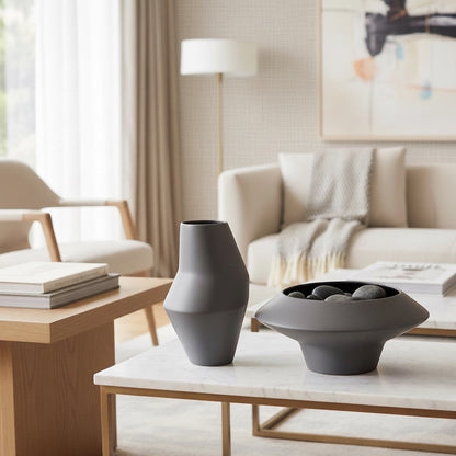 Eclectic wide matte grey ceramic vase with a low flared silhouette and dark interior on a marble coffee table.