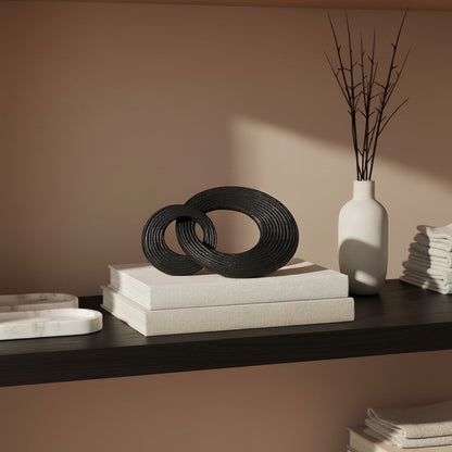 Eclectic metal ring decorative object set in matte black with textured finish displayed on books on a shelf.