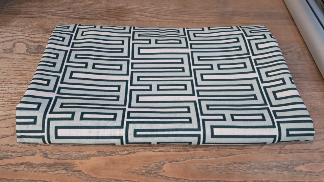 Eclectic mint green geometric tablecloth with a linen-look finish folded on a wooden table.