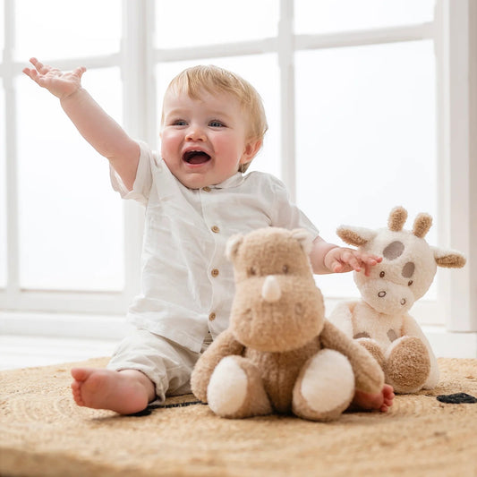 Eclectic Nattou cream and beige plush giraffe toy sitting next to a happy baby on a woven rug