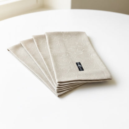 Eclectic set of four natural stonewashed linen napkins with a subtle tonal scroll pattern on a white table