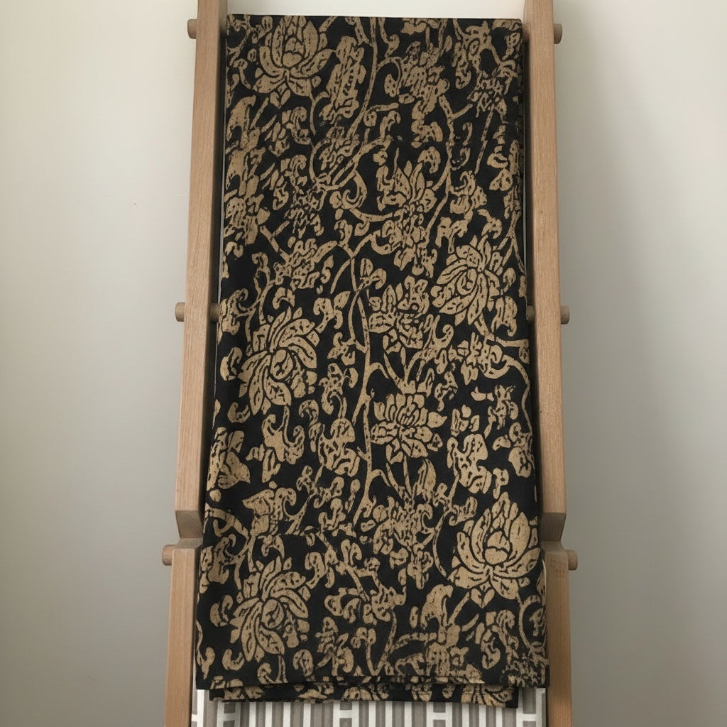 Eclectic Noir Baroque round tablecloth in black and gold with an intricate floral pattern draped over a wooden rack.