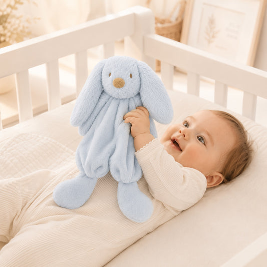 Eclectic Peluche powder blue bunny dou dou comfort blanket held by a smiling baby in a white crib