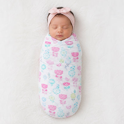 Newborn baby swaddled in an Eclectic cotton flannel blanket with a white and pastel floral print and pink headband.