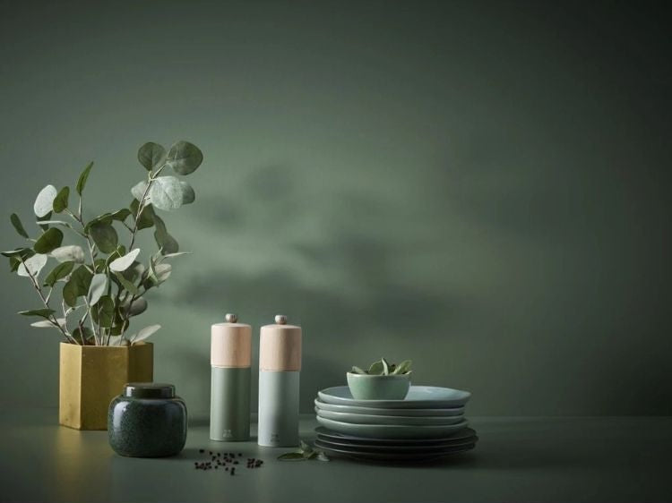 Eclectic Peugeot Boreal fern green and natural beechwood pepper mill set on a table with plates and a plant