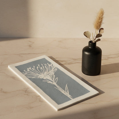 Eclectic Pincushion blue disposable airlaid napkin with a botanical protea print on a marble surface with a vase.