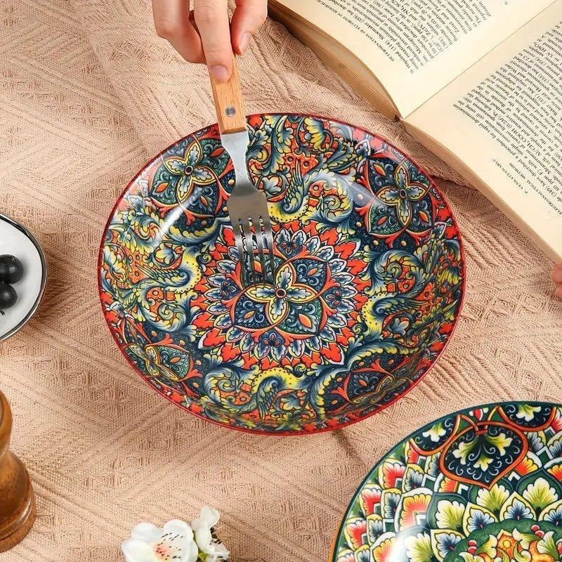 Eclectic red ceramic pasta bowl featuring a vibrant bohemian mandala pattern, shown with a fork on a textured cloth.