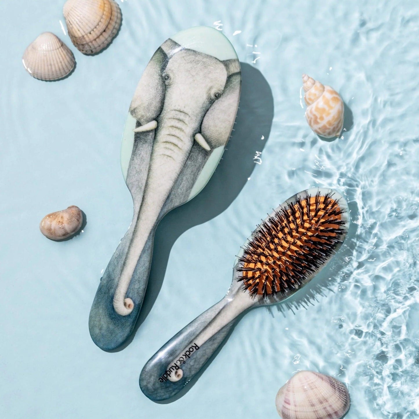 Eclectic Rock & Ruddle baby hairbrush with elephant illustration, featuring natural boar bristles on blue water.