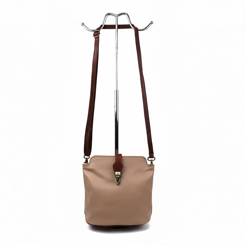 Eclectic Roma leather crossbody bag in beige with tan trim, gold hardware, and adjustable strap on a display stand.