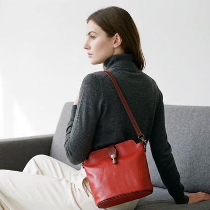 Model wearing a red Eclectic Roma leather crossbody bag with tan trim and gold hardware, seated on a grey sofa.