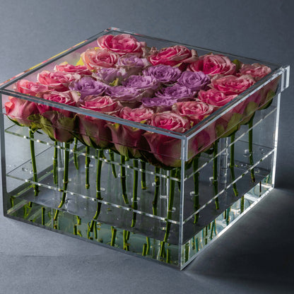Eclectic rose box featuring a square clear acrylic container filled with vibrant pink and purple roses