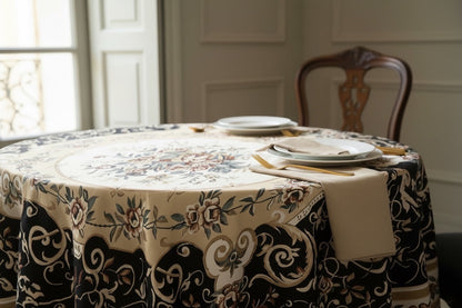 Eclectic round tablecloth featuring a vintage baroque floral pattern in black, gold, and ivory on a dining table.
