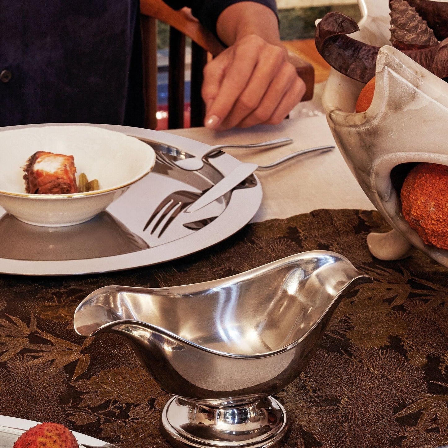 Eclectic Sambonet Elite oval sauce boat in mirror-polished stainless steel on a formal dining table setting.