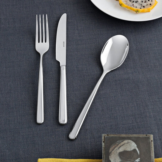 Eclectic Sambonet Linear mirror-polished stainless steel fork, knife, and spoon set on a dark grey textured tablecloth