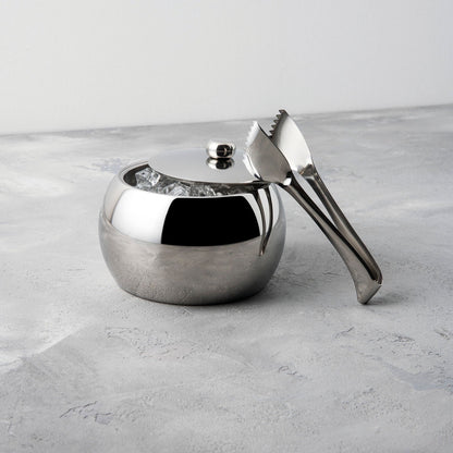 Eclectic Sambonet Living stainless steel ice bucket and tongs with a mirror-polished finish on a grey stone surface.