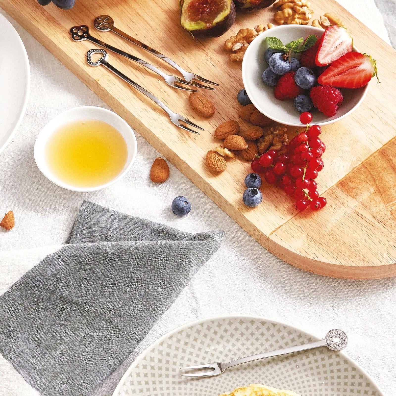 Eclectic Sambonet Party mirror stainless steel appetizer forks with decorative terminals on a wooden serving board.