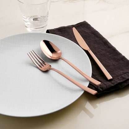 Eclectic Sambonet Rock mirror copper cutlery set with fork, spoon, and knife on a white plate and dark linen napkin.