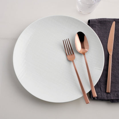 Eclectic Sambonet Rock mirror copper cutlery set with fork, spoon, and knife on a white plate and dark grey napkin.