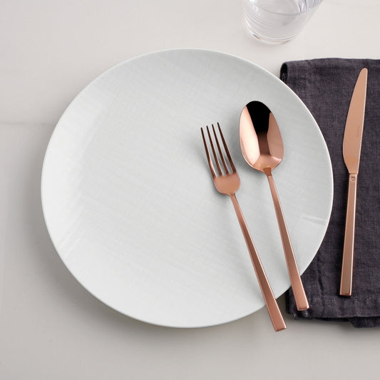 Eclectic Sambonet Rock mirror copper cutlery set with fork, spoon, and knife on a white plate and dark grey napkin.