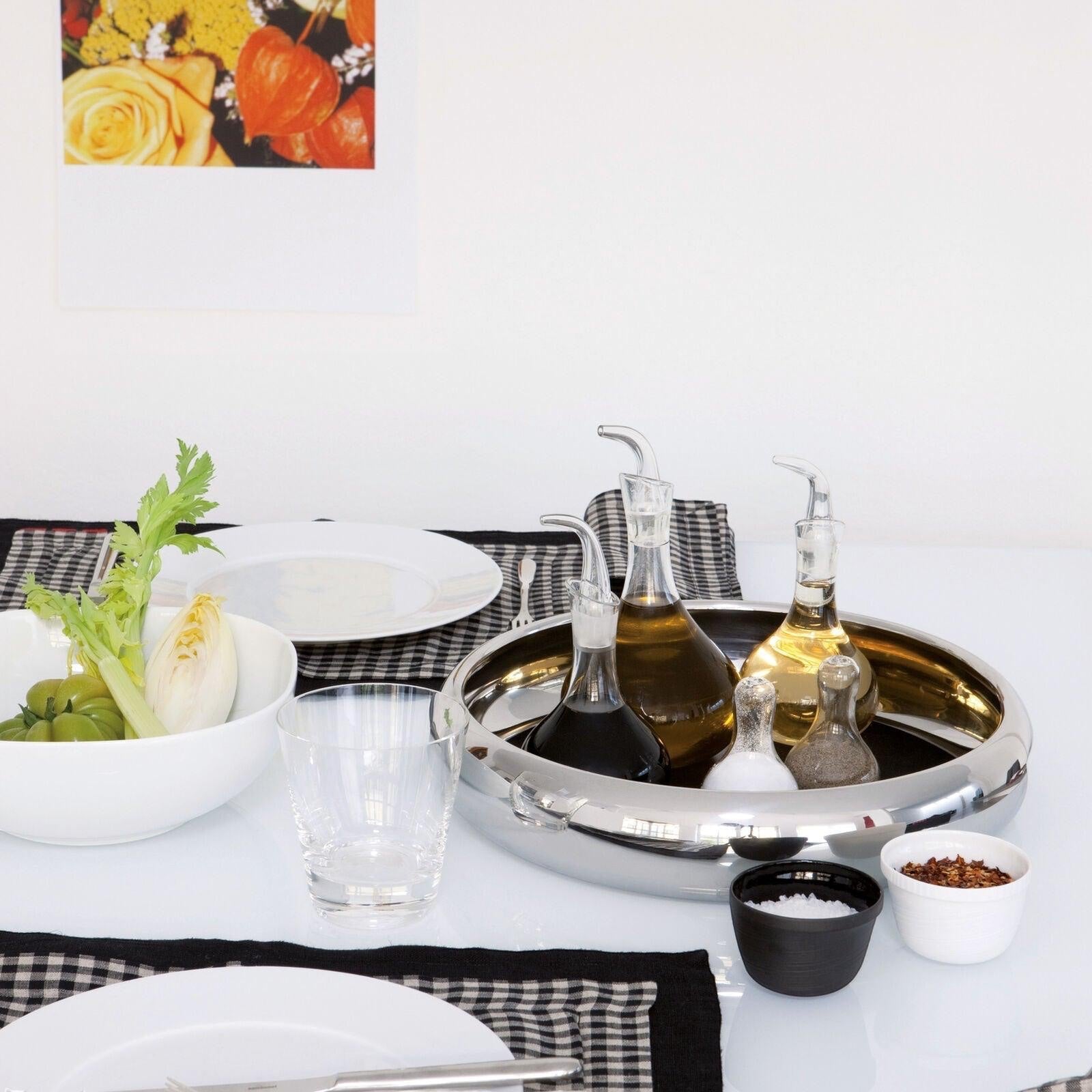 Eclectic Sambonet Sphera mirror-polished stainless steel serving bowl on a dining table with oil cruets and tableware.