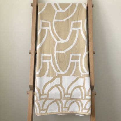Eclectic sand and white cotton tablecloth featuring a bold abstract pattern draped over a wooden ladder