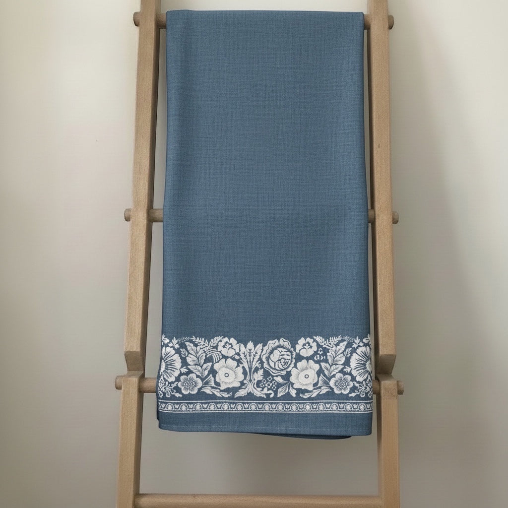 Eclectic soft blue linen-look tablecloth featuring a delicate white floral border pattern draped on a wooden ladder.