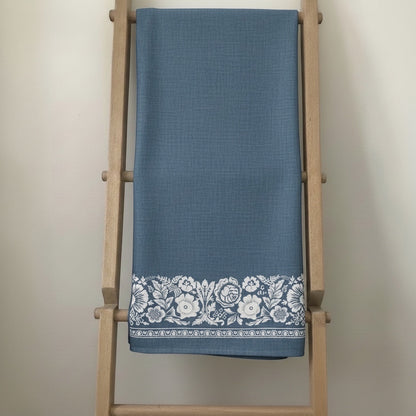 Eclectic soft blue linen-look tablecloth featuring a delicate white floral border pattern draped on a wooden ladder.