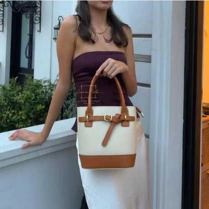 Eclectic Sorrento cream and tan grain leather crossbody bag with gold hardware held by a woman in a white skirt.
